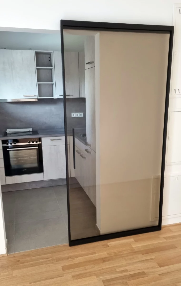 Glasschiebetür zur Küche in München-Neuhausen Maßgefertigte Glasschiebetür mit schwarzem Rahmen als transparente Raumtrennung vor einer Küche in München-Neuhausen.