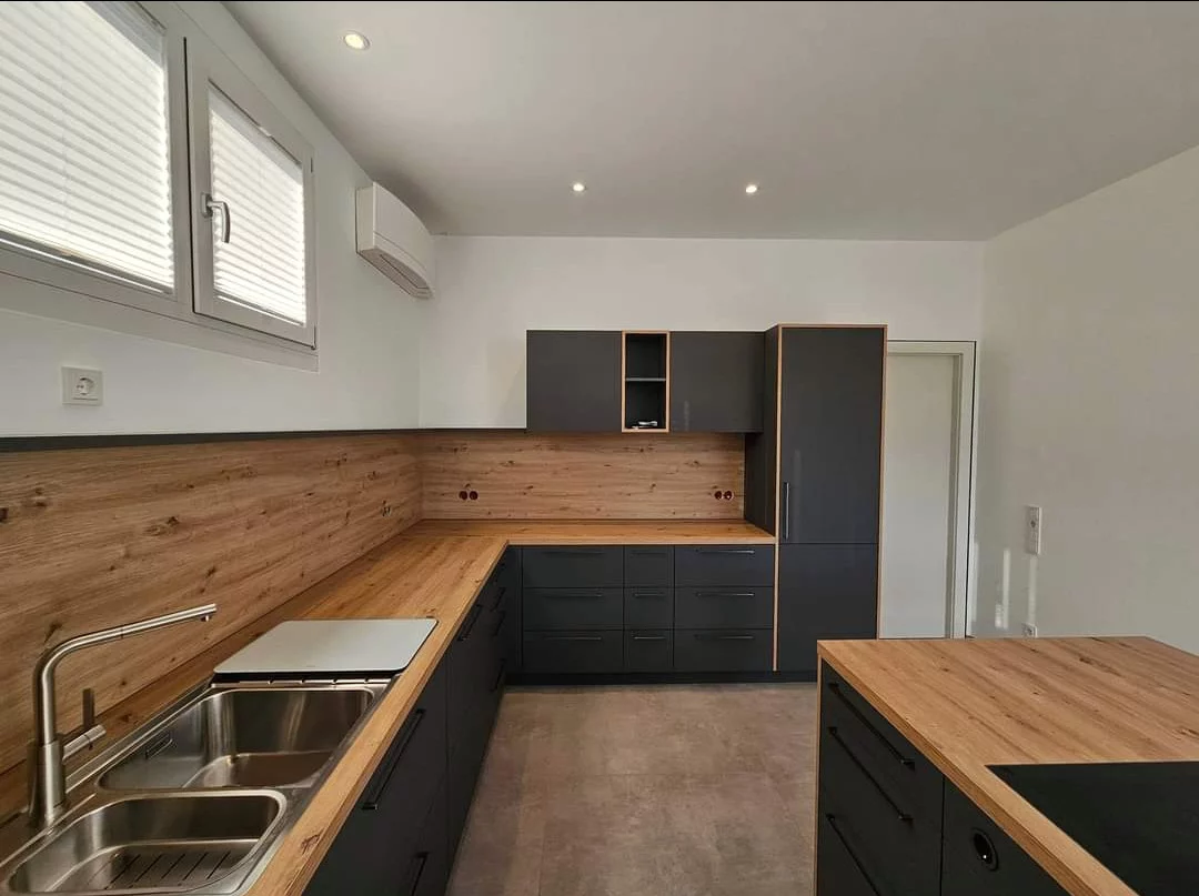 Moderne Küche nach Maß in Finsing Maßgefertigte Küche in Finsing mit dunklen Fronten, Holzarbeitsplatte, Holzrückwand und Kücheninsel.